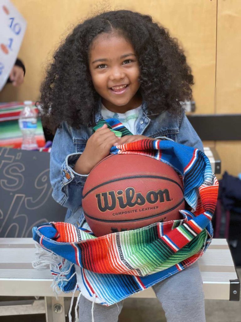 A child smiling and holding a basketball.