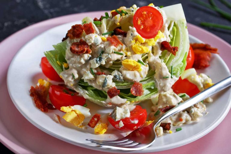 A wedge salad with tomatoes, bacon, crumbled blue cheese and hard boiled egg.