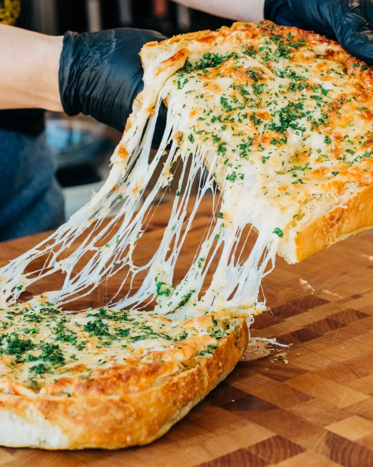 A person pulling a loaf of cheesy garlic bread apart