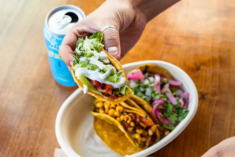 A close up of a hand holding tacos from the Co-op taqueria.