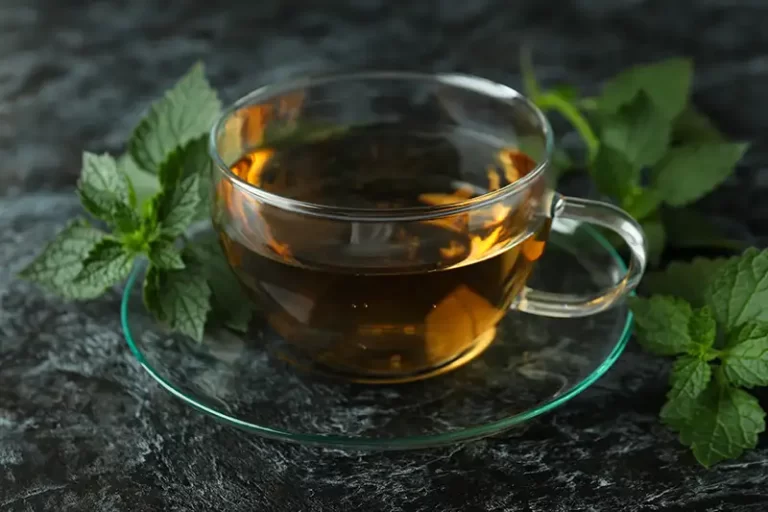 Nettle tea in a glass mug with fresh nettle leaves