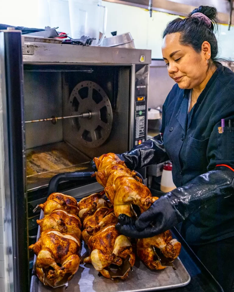 A Co-op employee removing cooked rotisserie chickens from the oven.