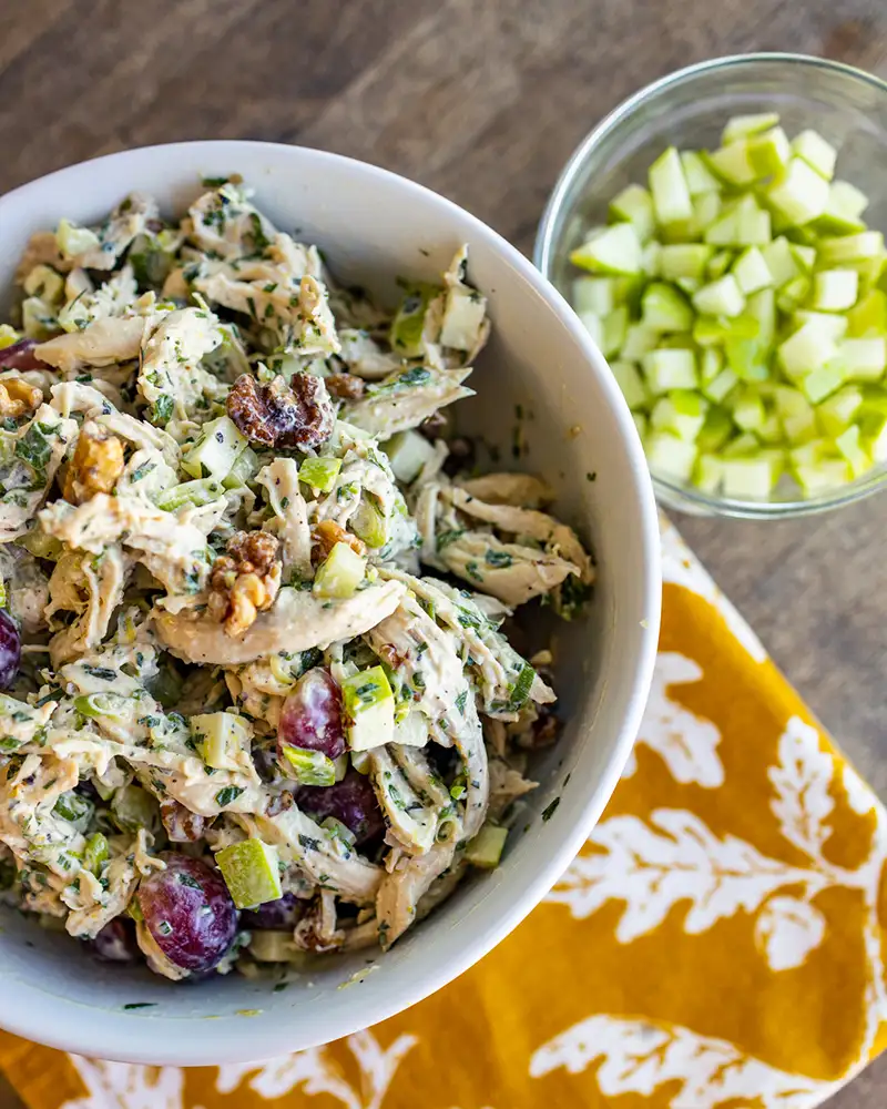 A waldorf chicken salad in a bowl on a yellow floral print cloth.