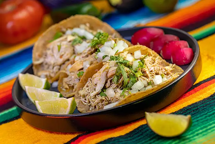Shredded chicken tacos on a colorful table cloth.