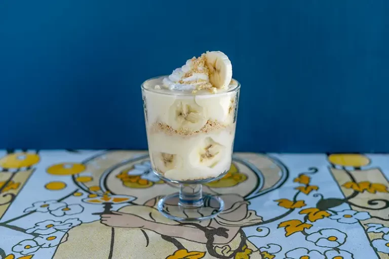 Banana parfait in a glass cup on a floral tablecloth.