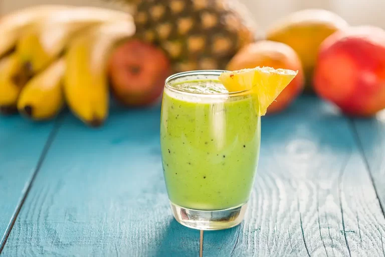 A green kale smoothie with a pineapple wedge garnish.