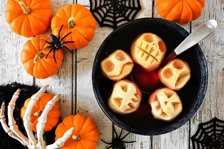 A table with Halloween decor and apples carved to look like shrunken heads in a bowl of cider.