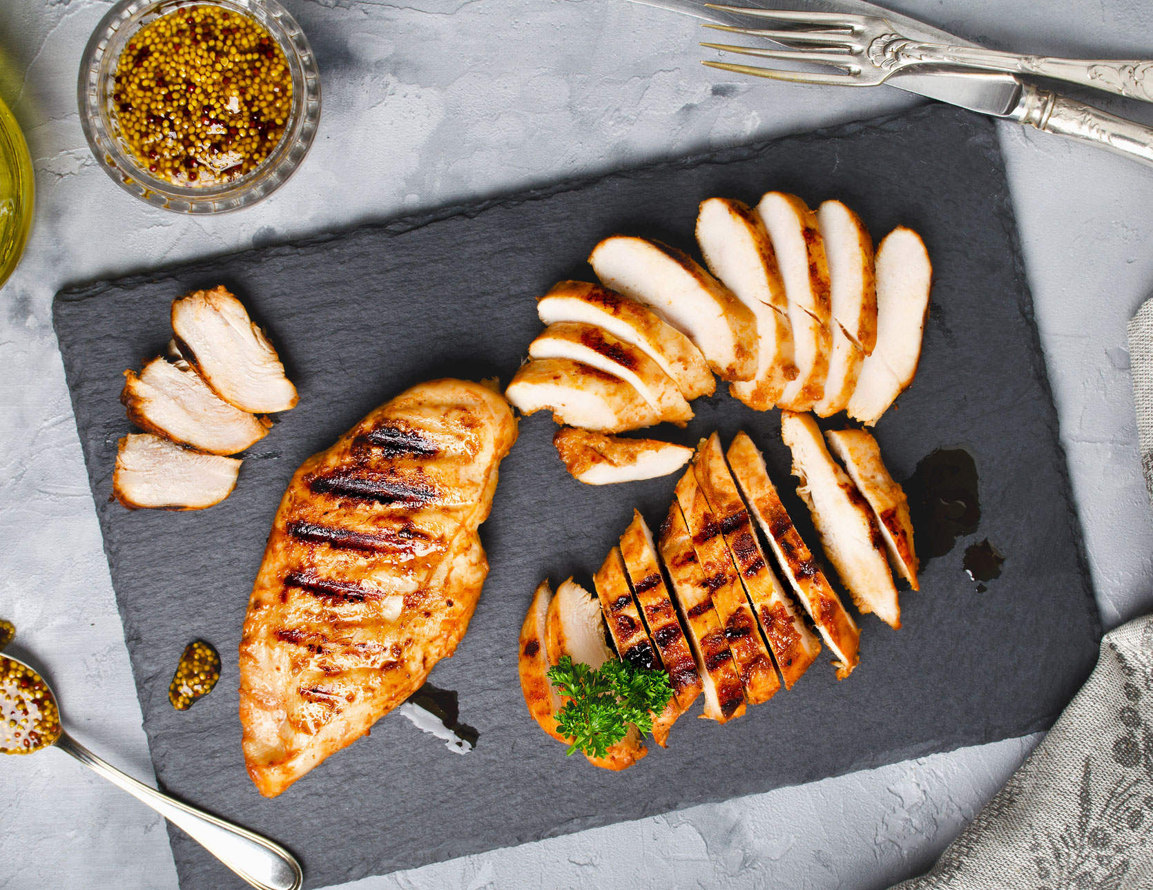 A piece of grilled chicken sliced into pieces on a cutting board.