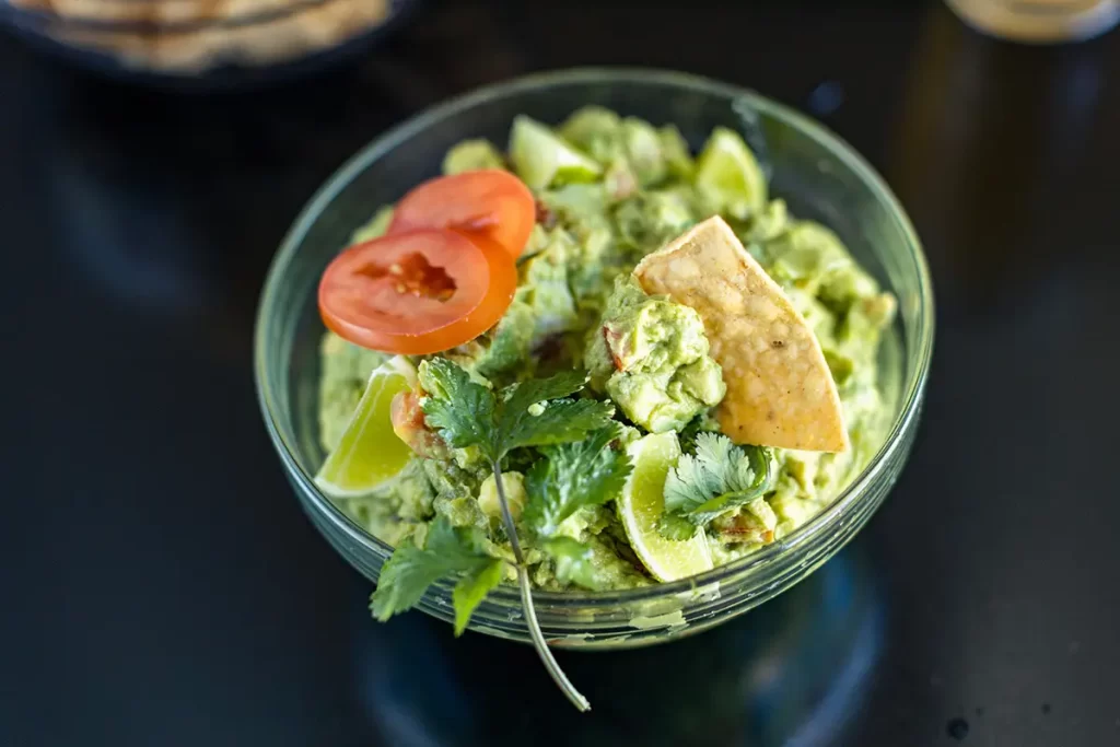 Guacamole in a bowl with a chip and fresh cilantro.