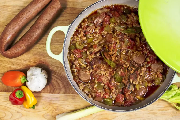 Pot of jambalaya on cutting board with andouille sausage, garlic, bell peppers and celery.