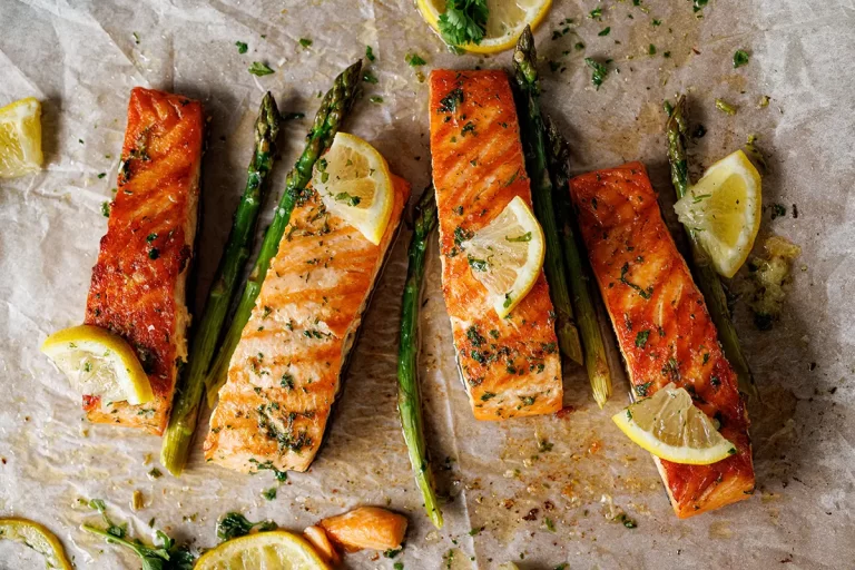Baked salmon fillets and green asparagus with aromatic herbs and lemon on baking paper