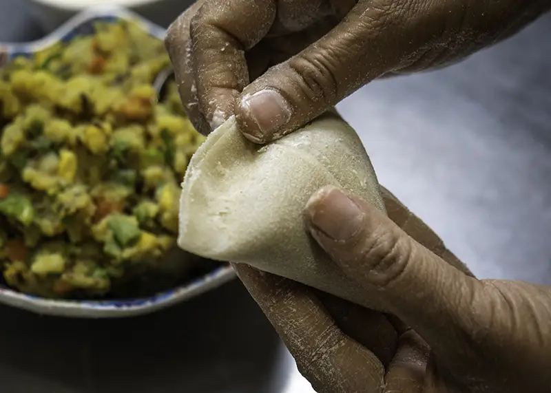 A close view of a hand making samosa dough.