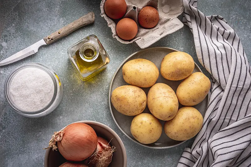 A top down view of potatoes, olive oil and other ingredients to make Tortilla Espanola.