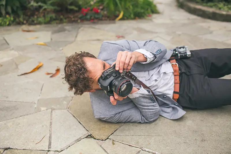 A well-dressed photographer laying on the ground while taking a photo.