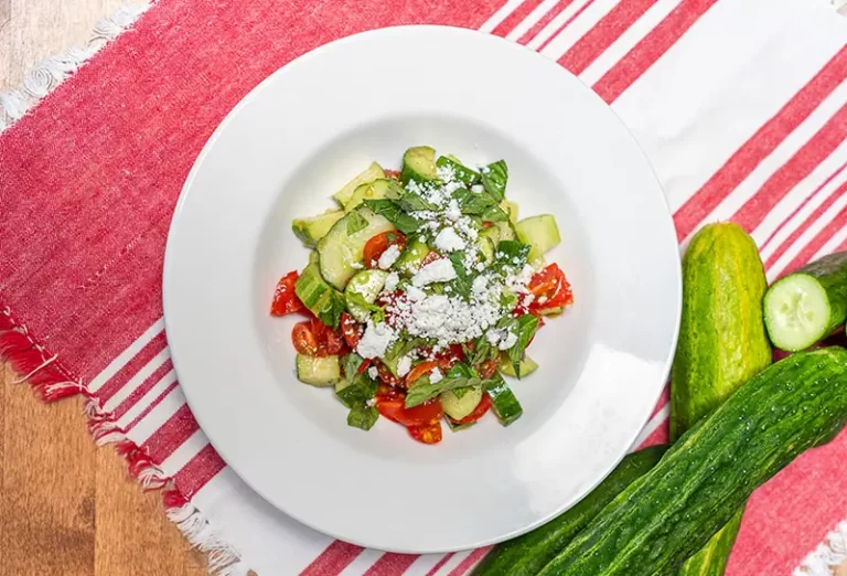 A cucumber and tomato salad with mint and feta on a plate.