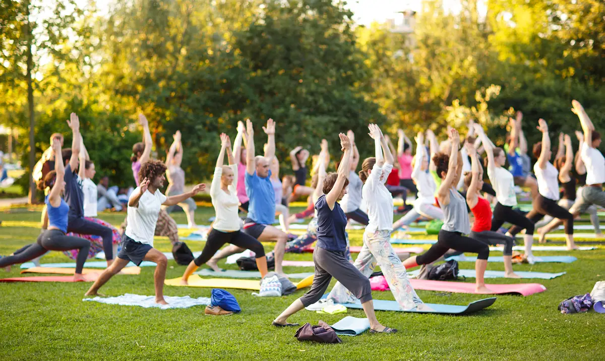Big group of adults attending a yoga class outside in park