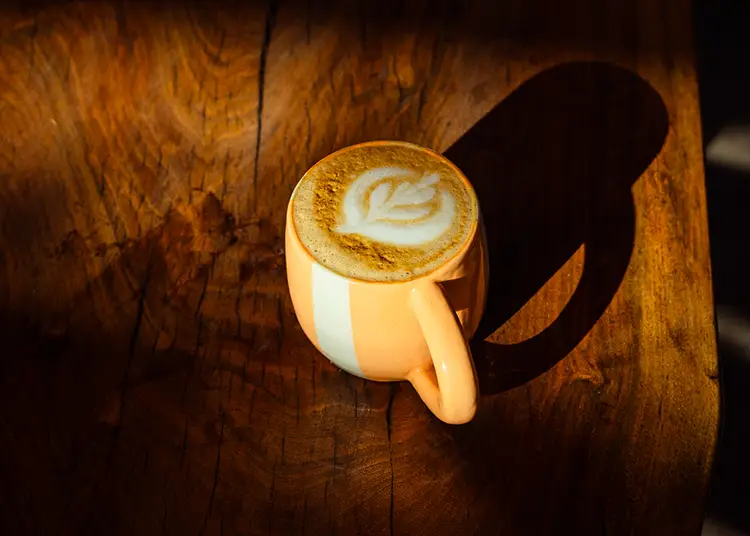 A latte in a yellow ceramic mug with foam art.