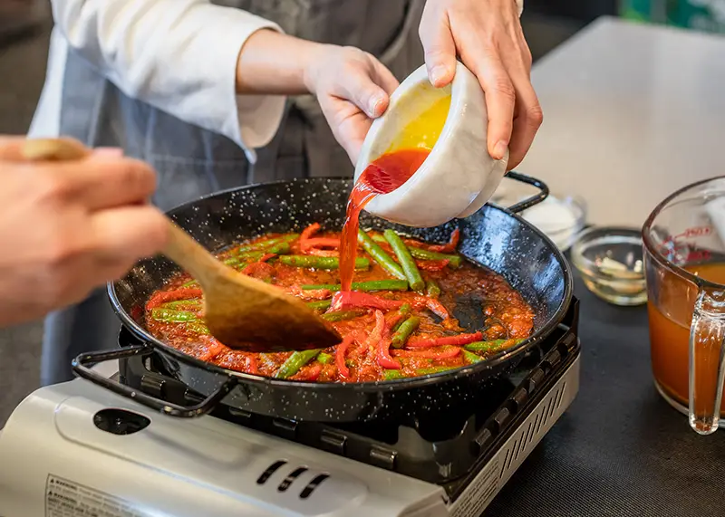 A red sauce being poured into a pan with green beans.