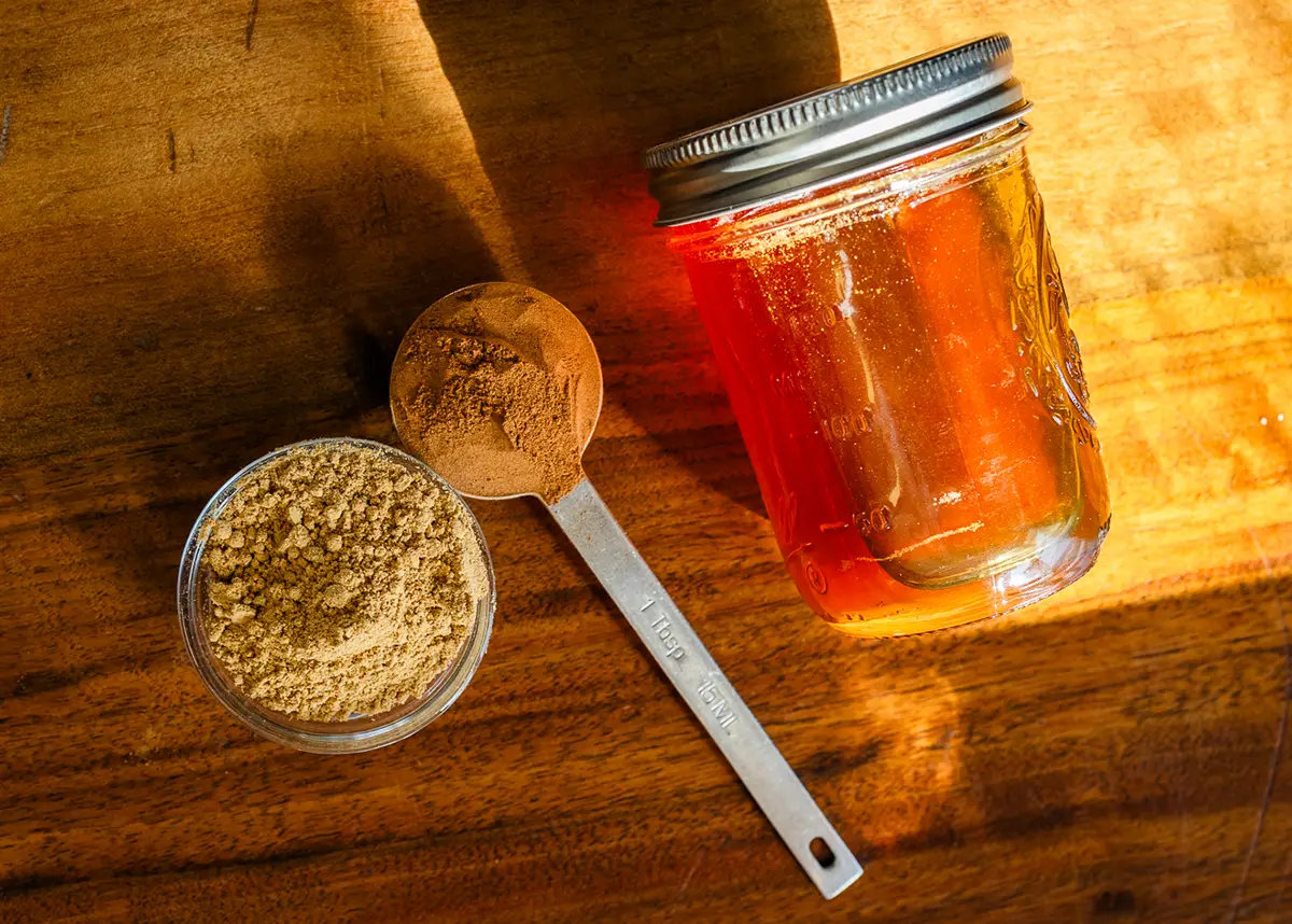 A jar of honey with spoonfuls of ginger and cinnamon.