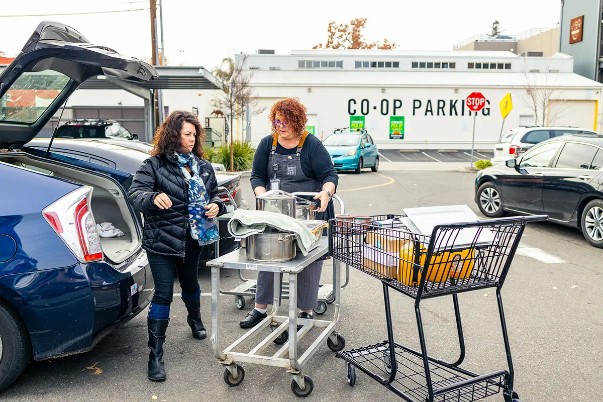 Linda and Lori loading food donations into a vehicle in the Co-op parking lot.
