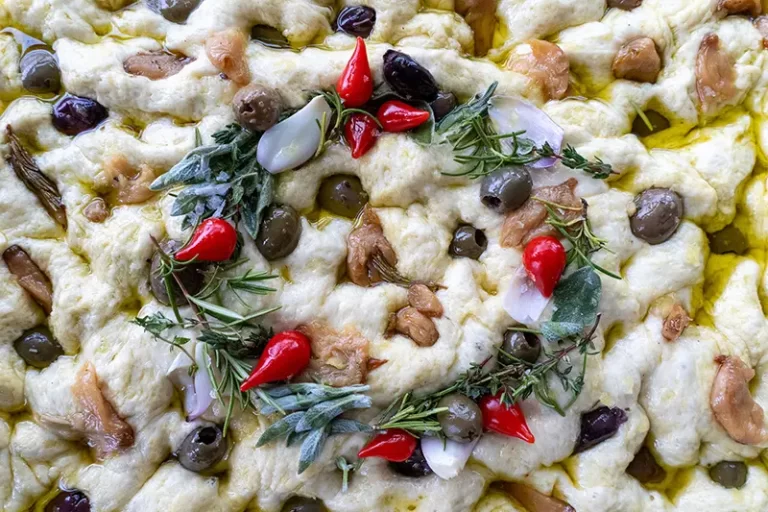 Raw focaccia dough decorated with a festive wreath of herbs and vegetables.