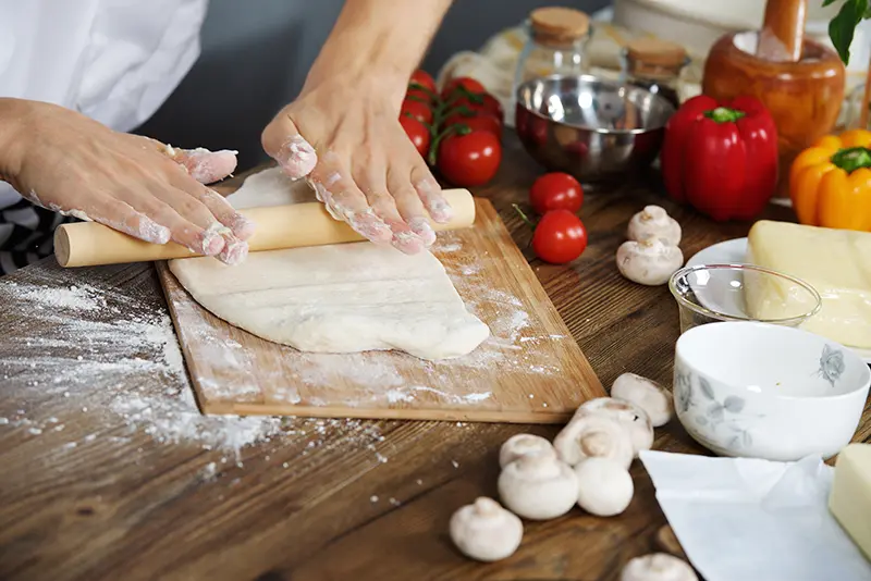 A person making pizza dough by hand on a cutting board.