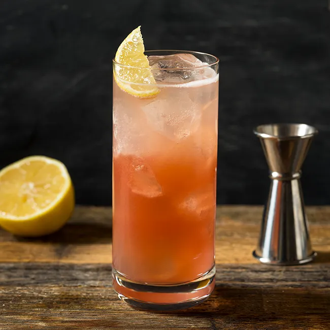 A vibrant cocktail in a tall glass with a slice of citrus.